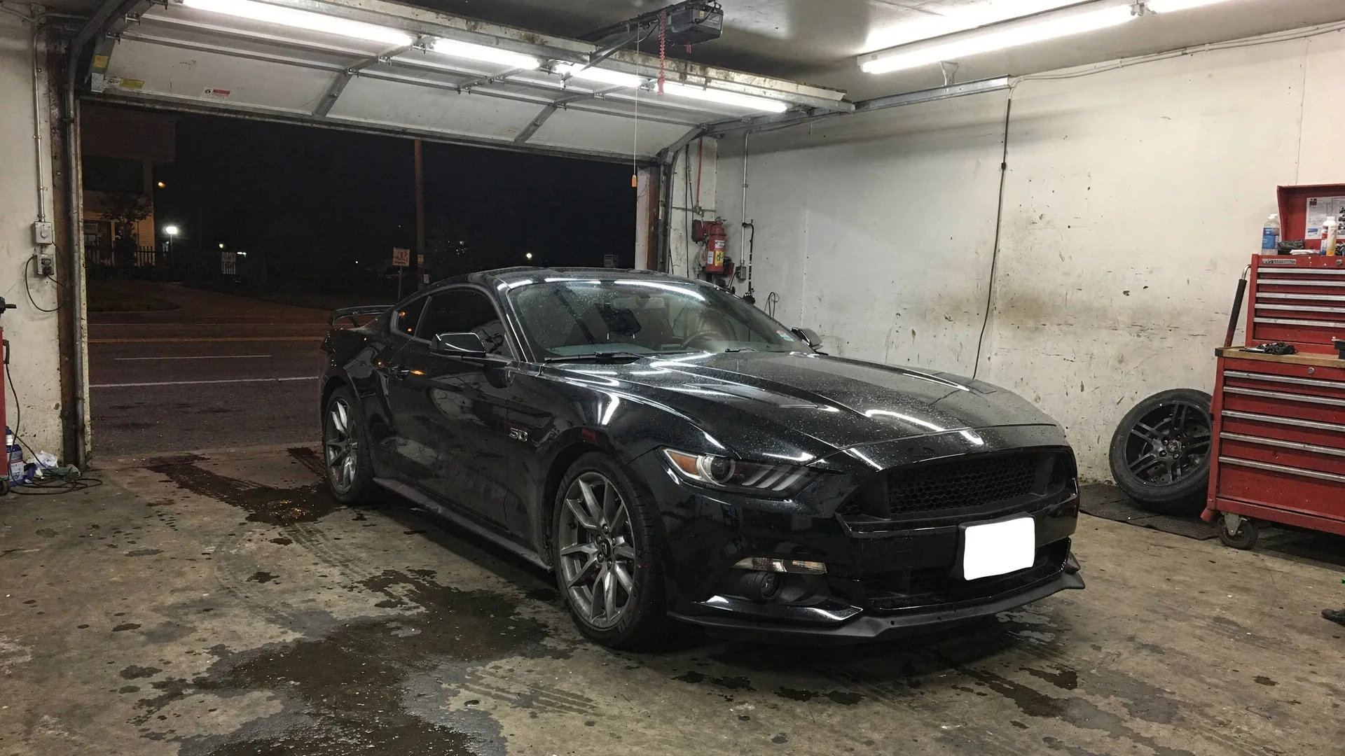 A black Ford Mustang GT in a small repair shop at night (AI placeholder photo)